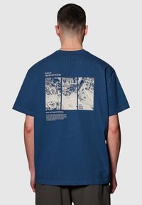 Mörkblå bomulls t-shirt med en vit grafisk tryck på baksidan som innehåller tre paneler och text, rund halsringning och korta ärmar.