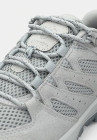 Svetlosivá turistická obuv z sieťoviny a semišu, s tenkými šnúrkami, polstrovaným golierom a textúrovanou gumovou podrážkou pre lepšiu trakciu.