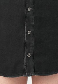Close-up of black denim skirt front with metal button closure and visible stitching above bare legs.