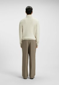 Maglione crema a collo alto con motivo a spina di pesce; abbinato a pantaloni larghi di colore marrone chiaro. Visibili dettagli in maglia testurizzata e vestibilità rilassata.