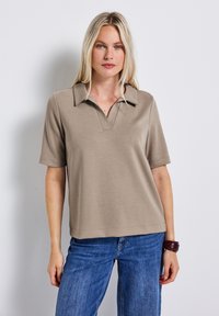 Lichtbeige polo met korte mouwen en een v-hals, met een soepele textuur en een losse pasvorm, gecombineerd met een blauwe jeans.