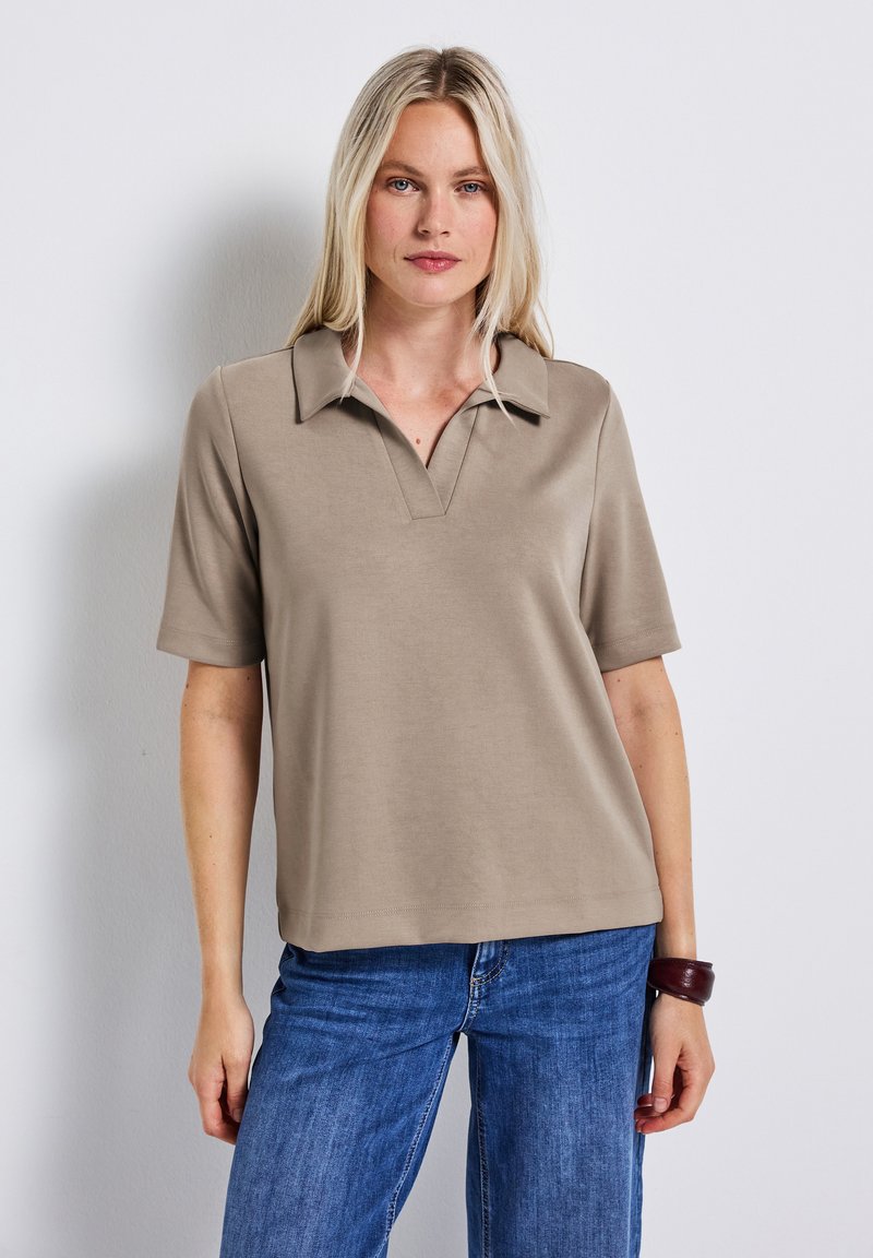Lichtbeige polo met korte mouwen en een v-hals, met een soepele textuur en een losse pasvorm, gecombineerd met een blauwe jeans.