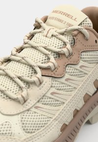 Chaussure de sport beige clair avec une tige en maille, accents roses et beiges, semelle intermédiaire en mousse injectée et lacets à motifs. Étiquette de la marque visible sur la languette.