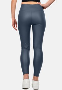 Hoge taille, strakkere leggings van een gladde, matte donkerblauwe stof. Bevat minimale stiksels en is gecombineerd met witte sportschoenen.