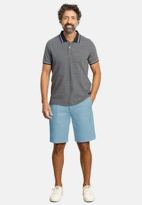 Camisa polo de hombre en cuadro azul marino, con un cuello sólido azul marino, combinada con pantalones cortos azul claro. Zapatillas blancas completan el atuendo.