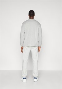 Γκρι μακρυμάνικη μπλούζα με στρογγυλή λαιμόκοψη, σε συνδυασμό με γκρι φόρμες σε μαλακό ύφασμα, φορώντας άσπρα αθλητικά παπούτσια.