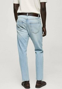Blugi din denim albastru deschis, cu croi drept, design cu cinci buzunare și o curea împletită maro. Purtați cu sandale maro, prezentând o vedere din spate.