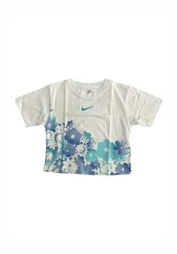 T-shirt bianca tagliata con un motivo floreale blu sul fondo e un logo Nike turchese sul petto. Realizzata in cotone.