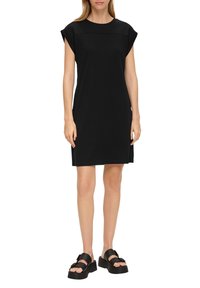 Musta lyhythihainen mekko, jossa on pyöreä pääntie, valmistettu pehmeästä kankaasta. Mekolla on rento istuvuus ja sivuhalkiot. Yhdistettynä paksupohjaisiin mustiin sandaaleihin.