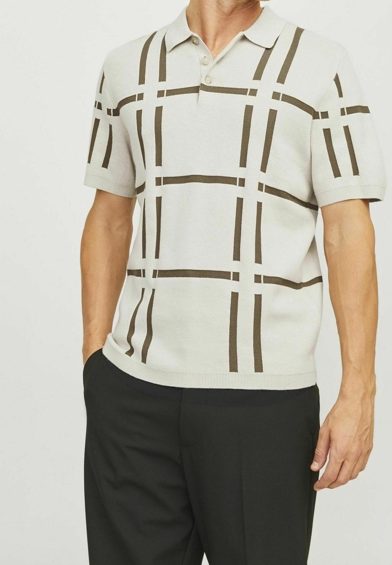 Kortärmad polo skjorta i krämfärg med mörkbrun rutmönster. Har en ribbad krage och knappar, tillverkad av ett strukturerat stickat material.