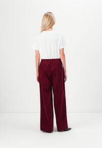 T-shirt blanche à manches courtes associée à un pantalon moulant bordeaux, avec une taille élastique et une coupe droite.