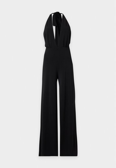 Combinaison noire sans manches à col halter avec jambes larges et profond décolleté en V noué au cou, présentée sur un fond uni.