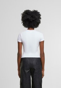 Camiseta blanca ajustada de manga corta, de tejido suave, con escote redondo, combinada con pantalones cargo negros texturizados con bolsillos traseros.