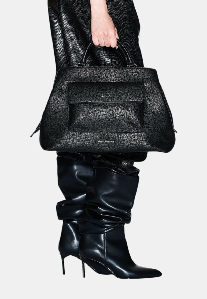 Borsa a mano in pelle nera con texture, dotata di doppi manici, con una tasca frontale e logo impresso, abbinata a stivali in pelle nera al ginocchio, morbidi.