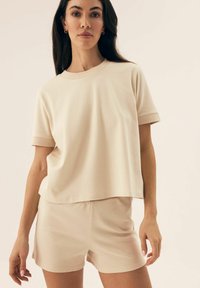 Beżowy, prążkowany top z krótkim rękawem z dopasowanymi szortami. Oba elementy mają luźny krój i wyraziste rękawy, wykonane są z miękkiego, lekkiego materiału.