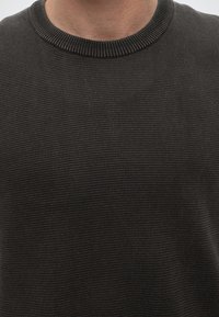Gros plan d'une personne portant un pull en maille côtelée gris foncé avec un col rond.