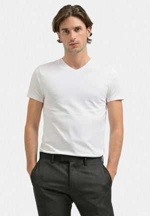 Hvid kortærmet V-hals t-shirt lavet af blød bomuld, parret med grå skræddersyede bukser. Glat tekstur, tætsiddende design.