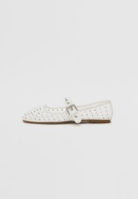 White flat shoe with a pointed toe, adorned with silver studs, features a buckle strap across the instep and a light brown sole.