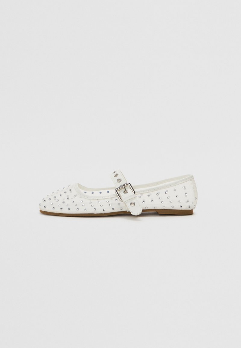 White flat shoe with a pointed toe, adorned with silver studs, features a buckle strap across the instep and a light brown sole.
