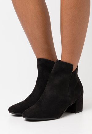 Bottines en daim noir avec un embout pointu, un petit talon bloc et des découpes sur les côtés, présentant une texture mate et un design simple.