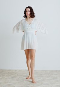 Abito bianco con scollatura a V, maniche in pizzo trasparente e vita arricciata. Vestibilità ampia e lunghezza al ginocchio, realizzato in un tessuto leggero e morbido.