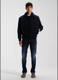 Ναυτικό bomber μπουφάν με μπροστινές τσέπες, φορεμένο πάνω από ένα μαύρο φούτερ με κουκούλα, σε συνδυασμό με σκούρο τζιν και γκρι αθλητικά παπούτσια.