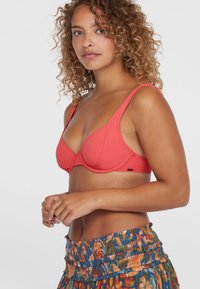 Korallfärgad bh med underwire, justerbara remmar, slät tyg och sömlös design. Modellen bär en flerfärgad mönstrad kjol.