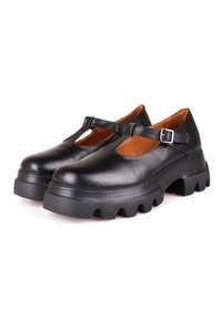 Paire de chaussures Mary Jane en cuir noir avec semelles plates-formes épaisses à rainures prononcées et brides réglables à boucle, présentées sur un fond blanc.