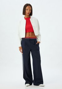 Chaqueta corta blanca, top rojo ajustado y pantalones de pierna ancha a rayas marino con franjas laterales. Texturas suaves, colores contrastantes y diseño casual.