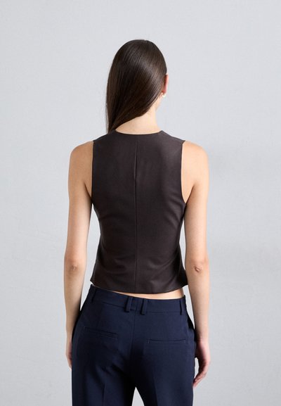 Dunkelbraunes, kurz geschnittenes ärmelloses Oberteil mit hohem Kragen und glatter Textur, kombiniert mit navyblauen, hochtaillierten Hosen.