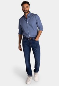 Blauw overhemd met kleine witte stippen, gecombineerd met donkere jeans en witte sneakers. Heeft een casual pasvorm en een kraag.
