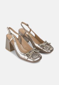Metallisch silberne Slingback-Absatzschuhe mit quadratischer Spitze, Blockabsatz und einer dekorativen Verzierung an der Vorderseite mit Strasssteinen.