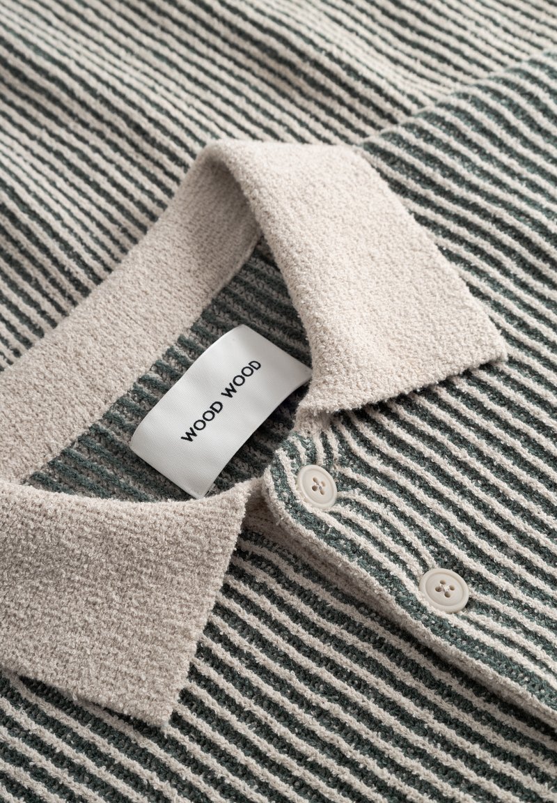 Striped polo shirt in green and beige, made of textured fabric. Features a beige collar, buttons, and a visible "WOOD WOOD" label.
