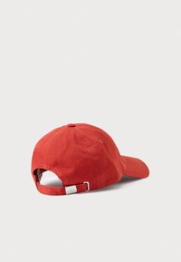 Red cotton cap with a curved brim, adjustable strap, and eyelet stitching. Features a simple, textured surface.