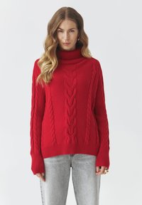 Czerwony sweter z golfem w sploty, wykonany z miękkiej przędzy, z grubymi ściągaczami przy mankietach i dolnym brzegu oraz z teksturowanymi wzorami biegnącymi wertykalnie na przodzie.