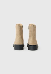 Botines de ante beige con un acabado liso y texturizado, cremalleras laterales y una gruesa suela de goma negra.