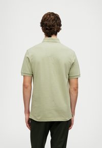 Camisa polo em verde claro, mangas curtas, colarinho clássico, feita de um tecido macio, vista traseira mostrando a bainha e fendas laterais.