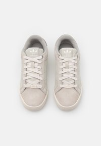 Vaaleanharmaat mokkaiset lenkkitossut, joissa on tasainen pinta, nauhallinen malli, pehmustettu kaulus ja valkoiset logoyksityiskohdat kielellä.