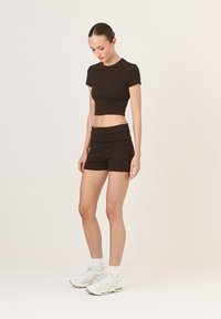 Fekete kötött crop top rövid ujjakkal, amelyhez illeszkedő magas derekú sort tartozik. A modellen fehér sportcipő és bokazokni található.