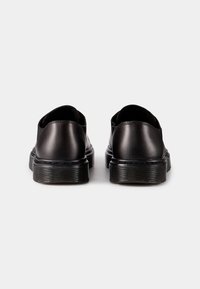 Des chaussures noires en cuir, à enfiler, avec une finition lisse, un orteil arrondi et une semelle en caoutchouc texturé. Design minimaliste, sans matériel ou accents visibles.