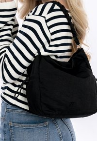 Zwarte schoudertas van zacht stof met een slouchy ontwerp, voorzien van een gevlochten schouderriem en een subtiele logo-accent. Casual en functioneel.