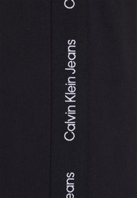 Tessuto elasticizzato nero con un dettaglio verticale bianco "Calvin Klein Jeans" sul lato. Texture liscia e design slim fit.