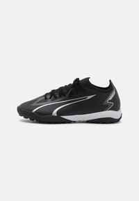 Botas de fútbol negras y blancas de corte bajo con suela texturizada, cordones y diseño de swoosh plateado en el lateral, diseñadas para jugar en césped artificial.