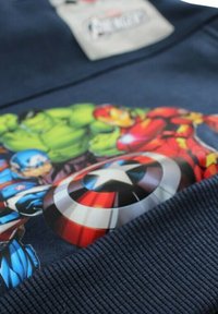 Sweat-shirt bleu marine avec un graphique vibrant de plusieurs super-héros et le bouclier de Captain America, texture côtelée le long de l'ourlet.