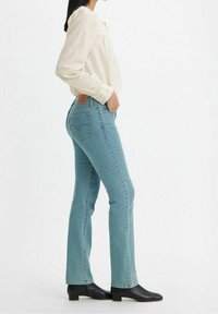 Jean en denim bleu clair, à taille ajustée, jambe évasée et surpiqûres discrètes. Associe à un chemisier crème et des bottines noires.