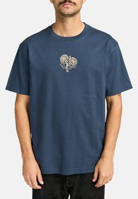 Marineblaue Baumwoll-T-Shirt mit Rundhalsausschnitt und kurzen Ärmeln, mit einem hellbeigen Blumenmuster in der Mitte.