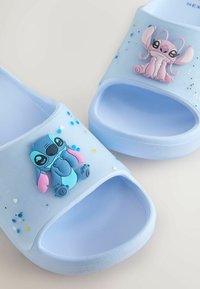 Sandale cu talpă albastră, cu personaje 3D, unul albastru și unul roz, cu puncte colorate împrăștiate pe o baretă translucidă. Talpă texturată.