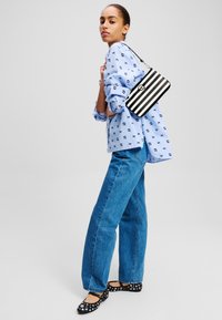 Sac rayé noir et blanc, chemise à motifs bleus, jean bleu ample et ballerines noires à pois blancs. Tenue simple et décontractée.