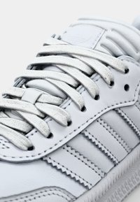 Weiße Ledersneaker mit flachen Schnürsenkeln, strukturierten Seiten mit drei Streifen und einer gepolsterten Zunge mit geprägtem Logodetail.