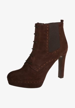 Stivaletto alla caviglia con tacco alto in suede marrone, con allacciatura frontale, pannello elastico laterale, perforazioni decorative e suola platform.